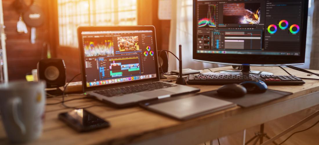 Laptop and external monitor on wooden desk with Adobe programs on screens