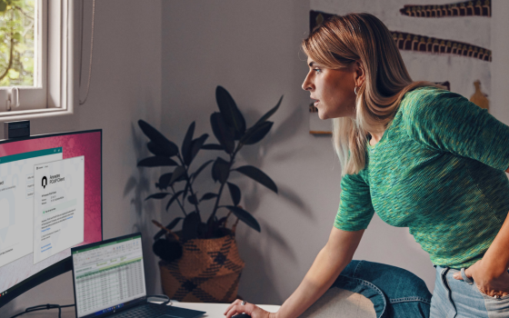A woman leaning over a desk with her hand on a mouse, looking at a monitor showing HP Anyware applications.
